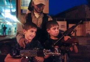 An ISIL Takfiri militant stands with two children posing with weapons in Iraq’s northern city of Mosul.