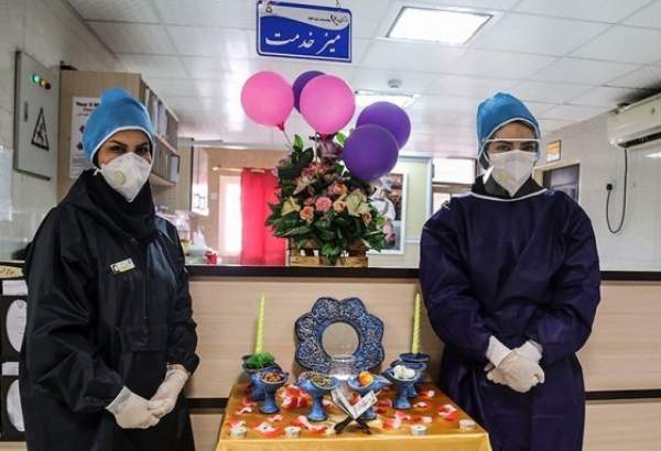 Two Iranian nurses in coronavirus-infection ward, standing next to Haft Seen set, traditional set of items laid to mark beginning of the Persian New Year as the country is challenged by COVID-19 on the eve of the New Year 1399. (Photo: Tasnim)
